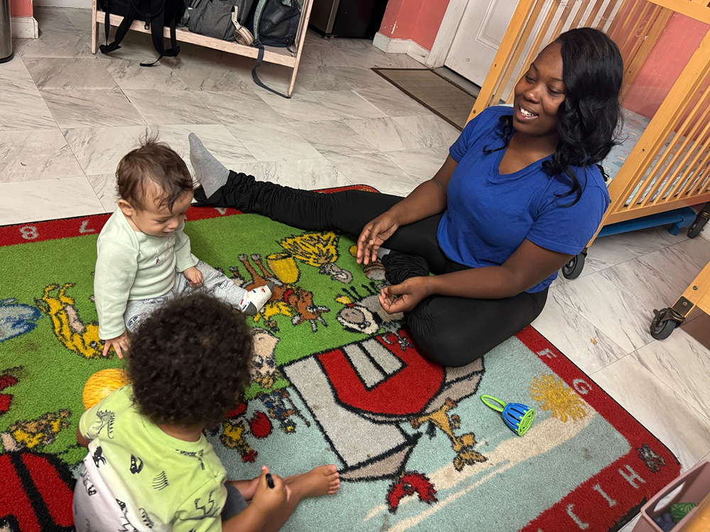 A woman and two children happily interact while playing on a soft rug, surrounded by a cheerful indoor environment.