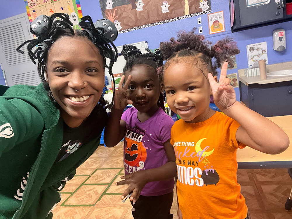 In a classroom, a woman interacts with two children, fostering a supportive and educational environment.